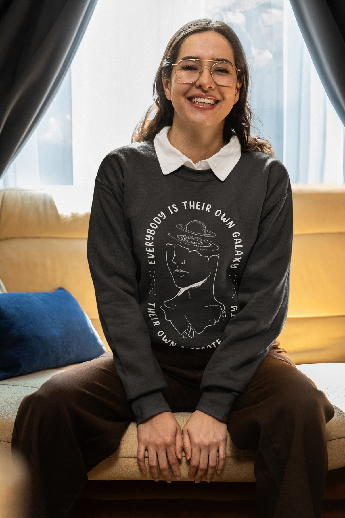 'Everybody Is Their Own Galaxy' illustrated sweatshirt in black, woman sitting indoors on a couch, cozy gift