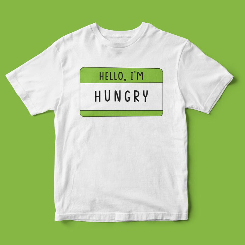 A white "Hello, I'm Hungry T-Shirt" displayed on a green background, showcasing a geeky name tag design with green borders. The text reads, "HELLO, I'M HUNGRY.