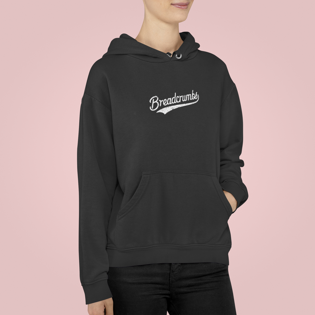 'Breadcrumbs' hoodie in dark heather, man wearing it against a pink backdrop, funny retro script logo gift