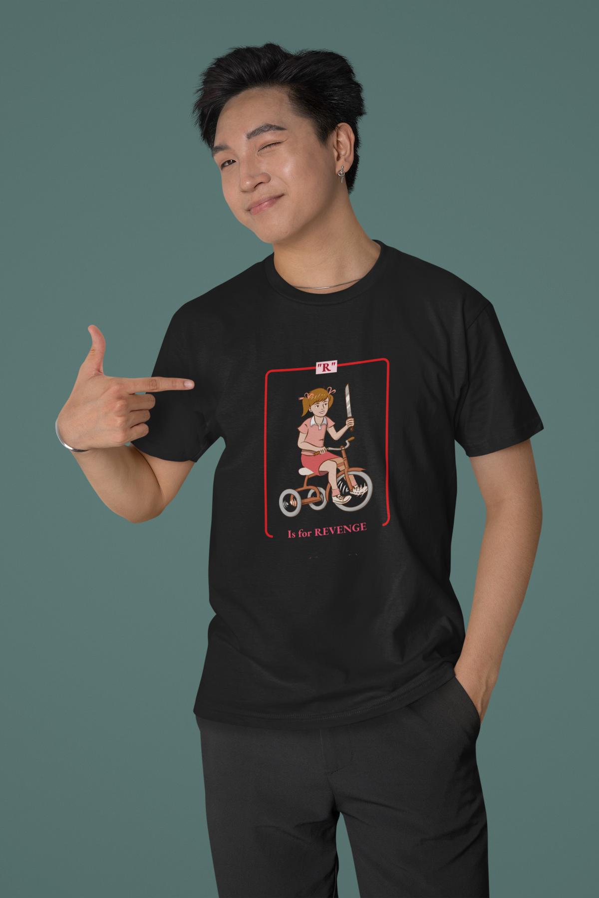 'R is for Revenge' tricycle girl graphic t-shirt in black, man pointing at print, teal backdrop, funny gift