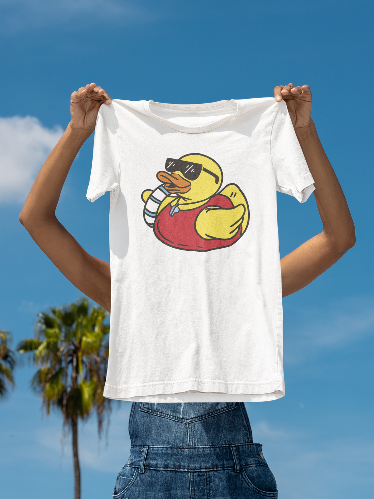 Life saver duck t-shirt in white, held up outdoors against a palm tree sky backdrop, funny beach gift