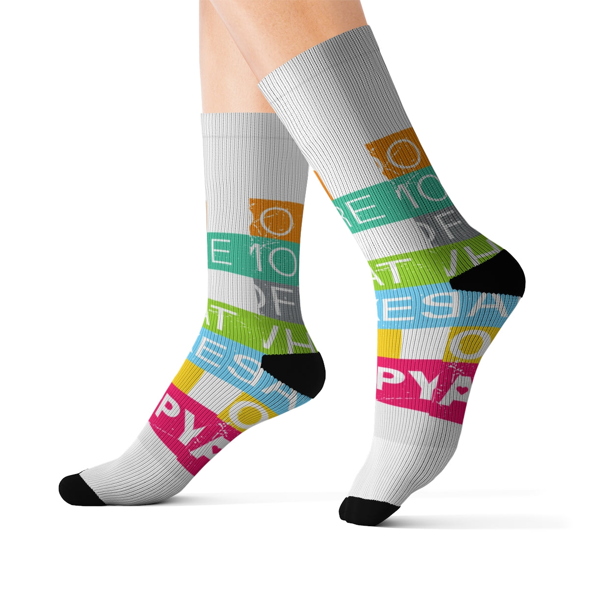 Feet in white crew socks with black toes and heels, decorated with colorful stripes and the phrase “Do More of What Makes You Happyâ€â€”ideal for anyone who loves fun socks and positive vibes.