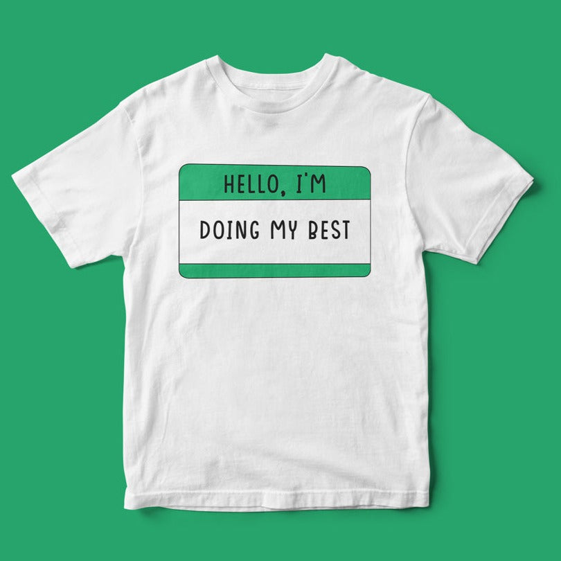 Get into a positive mindset with the "Hello, I'm Doing My Best" T-shirt—a white shirt adorned with a printed green name tag design that joyfully displays its uplifting message on a vibrant green background.