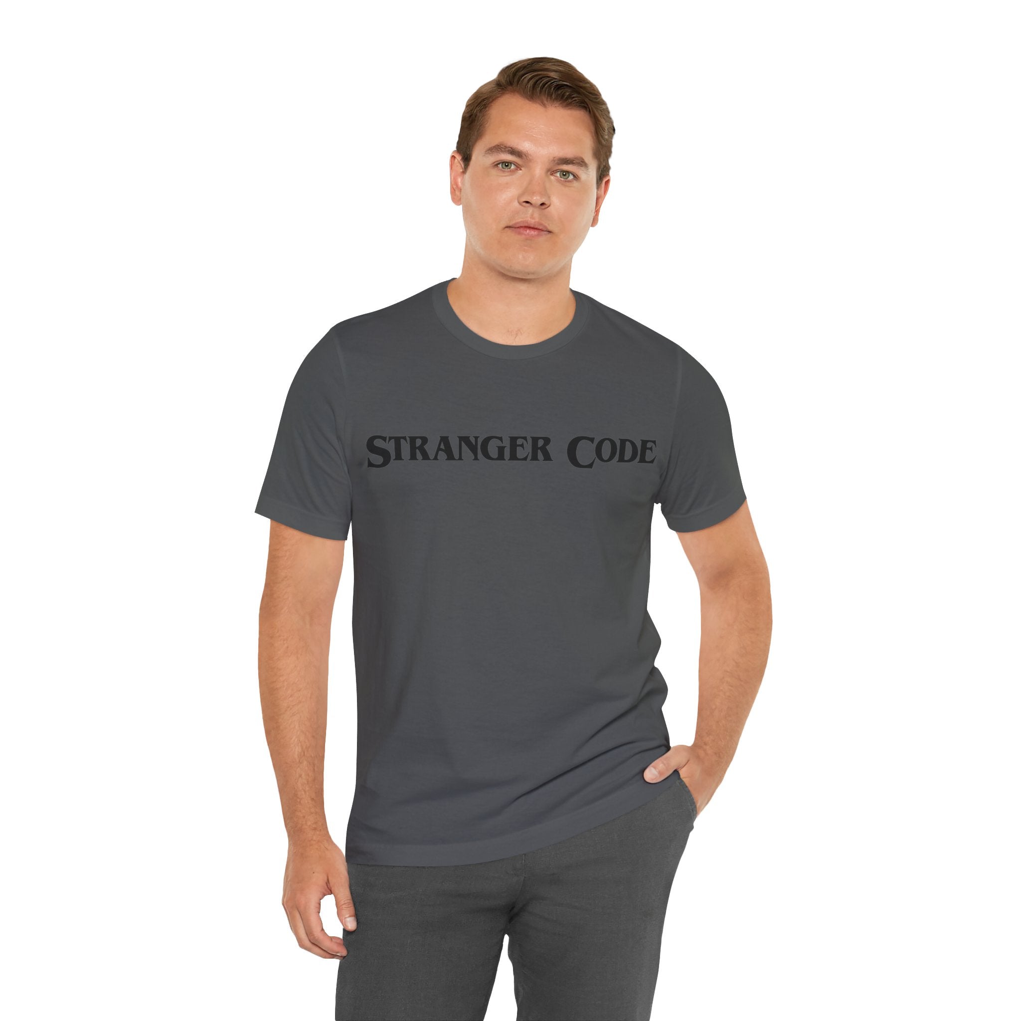 A person wearing the Stranger Code Tee Shirt in dark gray, paired with gray pants, stands against a white background, displaying the quality print on the soft cotton fabric.