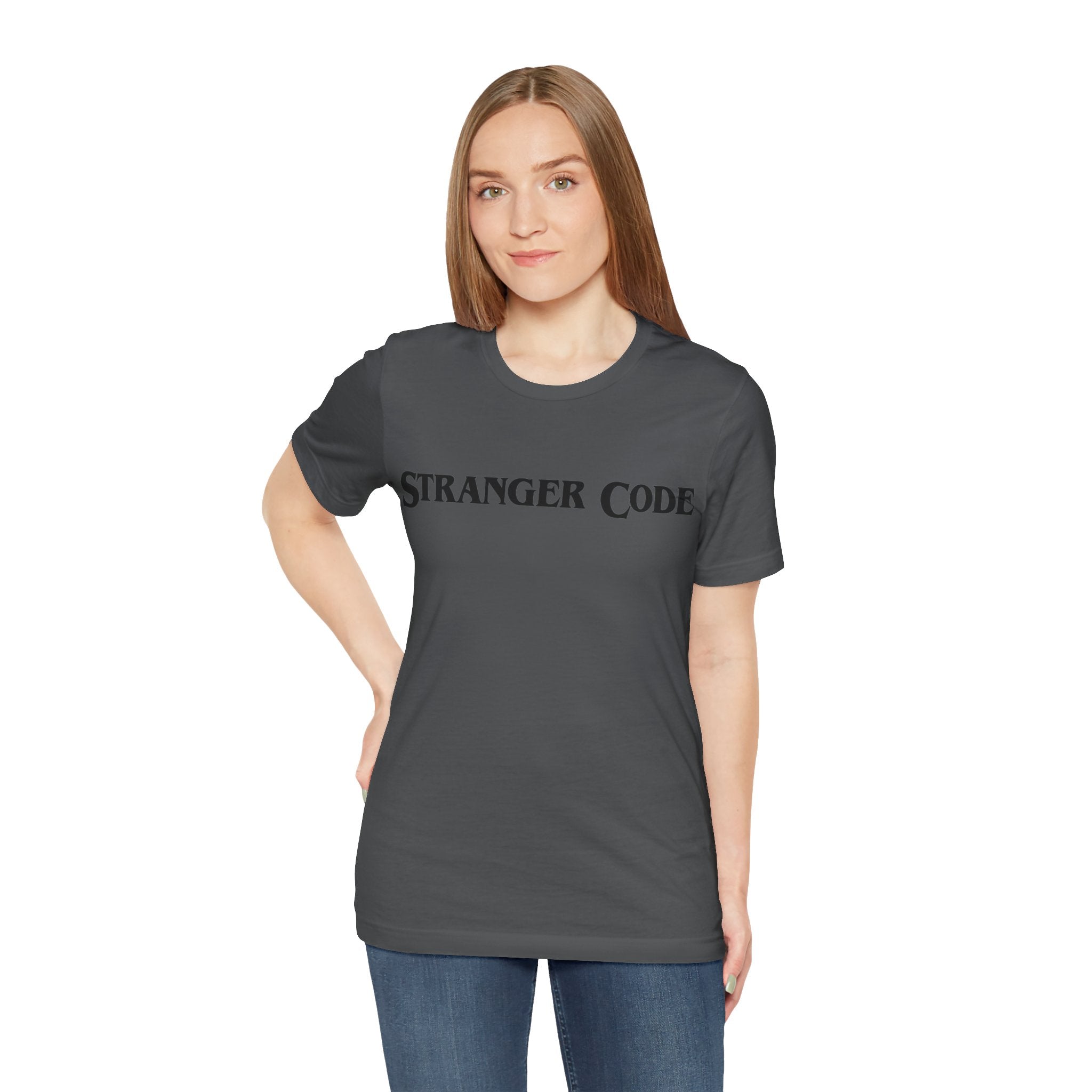 A person wearing a Stranger Code Tee Shirt, in dark gray with "STRANGER CODE" printed on the front, crafted from soft cotton, posing against a plain white background.
