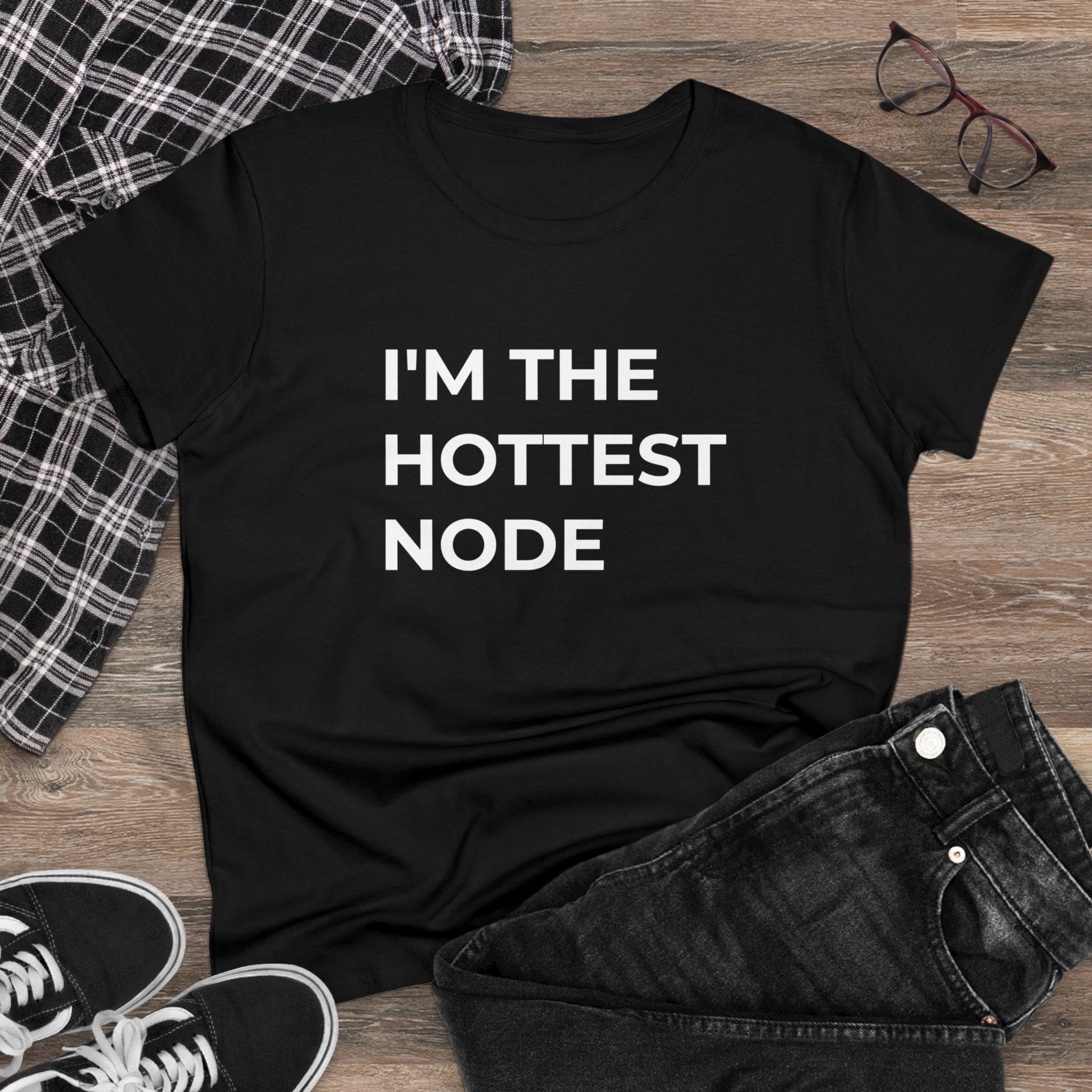Laid flat on a wooden surface, surrounded by a plaid shirt, glasses, and sneakers is the "I'm The Hottest Node - Women's Tee," an elegant black T-shirt. Elevate your fashion game with this premium cotton tee that delivers both comfort and style.