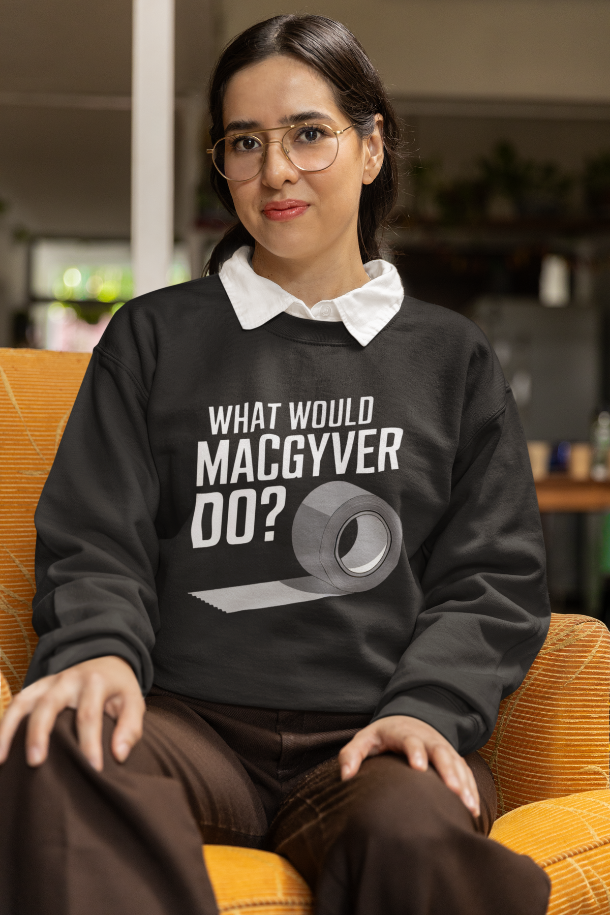 What Would MacGyver Do black sweatshirt worn by a woman sitting in a chair, cozy lifestyle photo