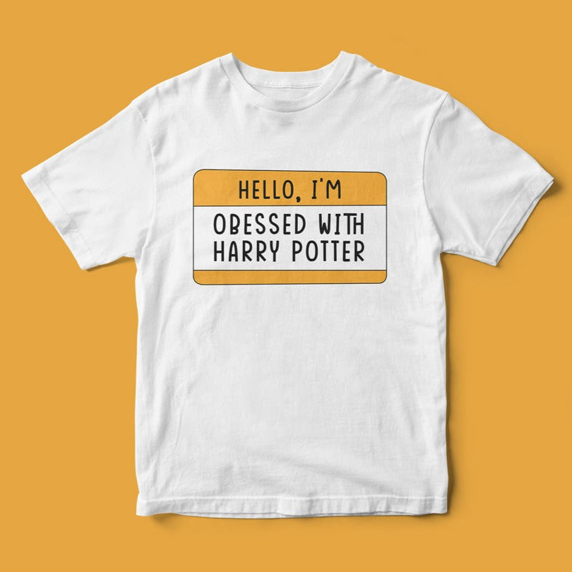 The "Hello, I'm Obsessed With Harry Potter" T-Shirt showcases a name tag design with the bold statement on a yellow background. Ideal for fans of the wizarding world, this tee is both fashionable and a playful tribute to your magical fandom.
