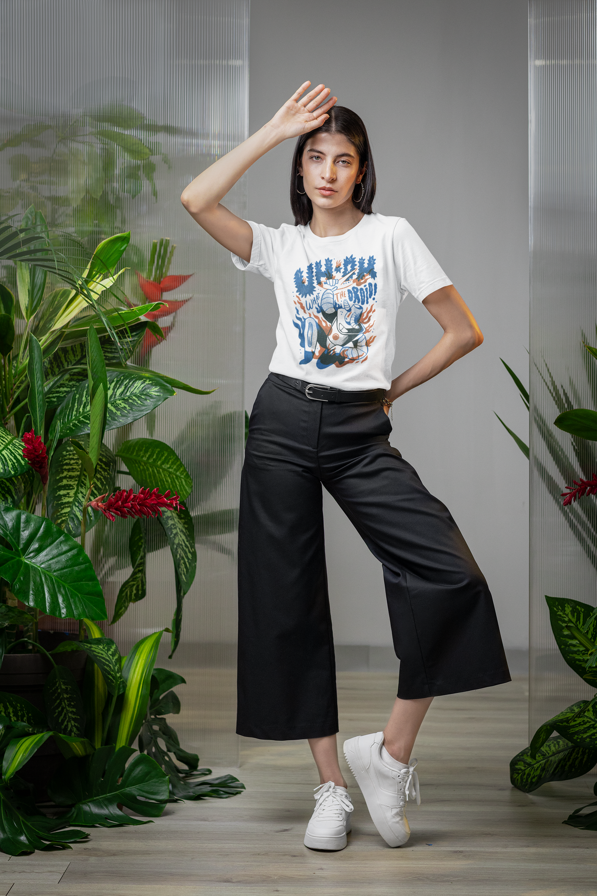 'Uh-Oh' droid attack t-shirt in white, woman model wearing it with black pants in a plant-filled room