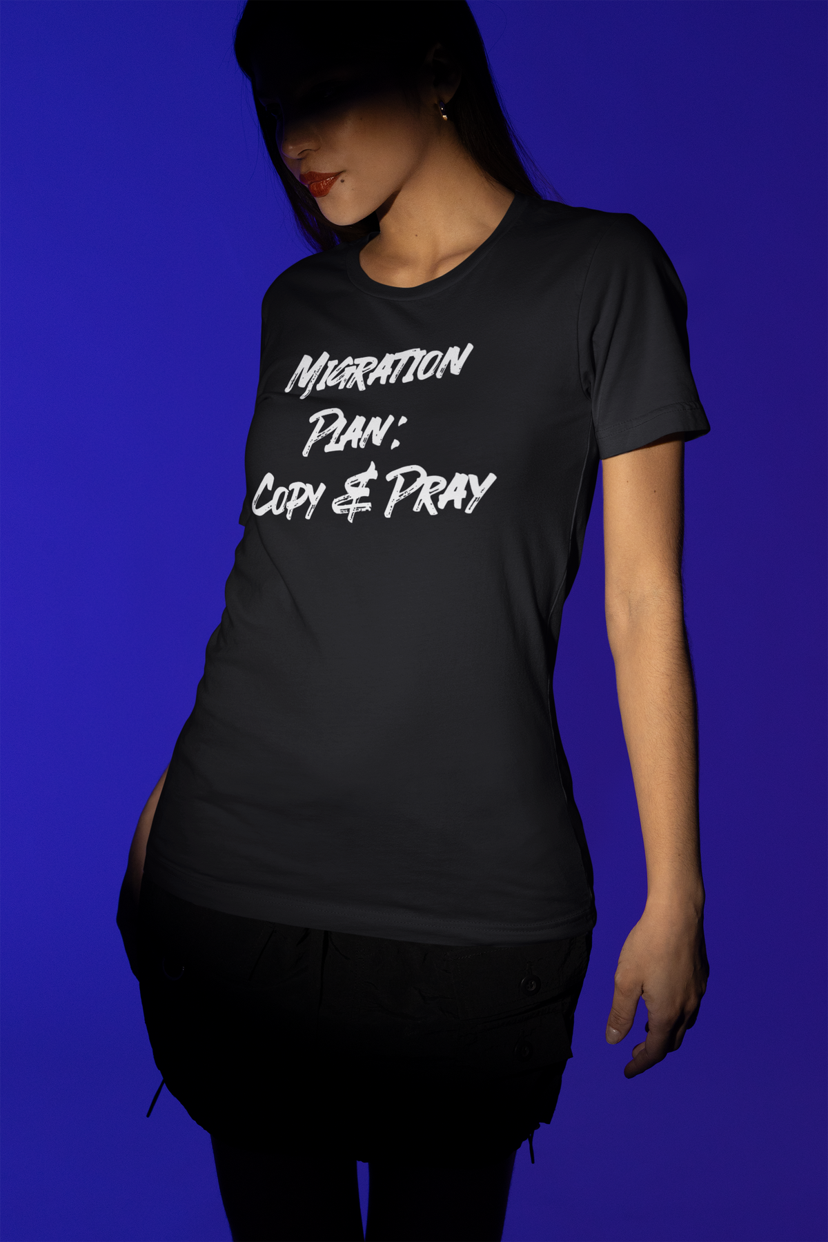 'Migration Plan: Copy and Pray' t-shirt in black, woman under blue stage lighting, funny it gift for coders