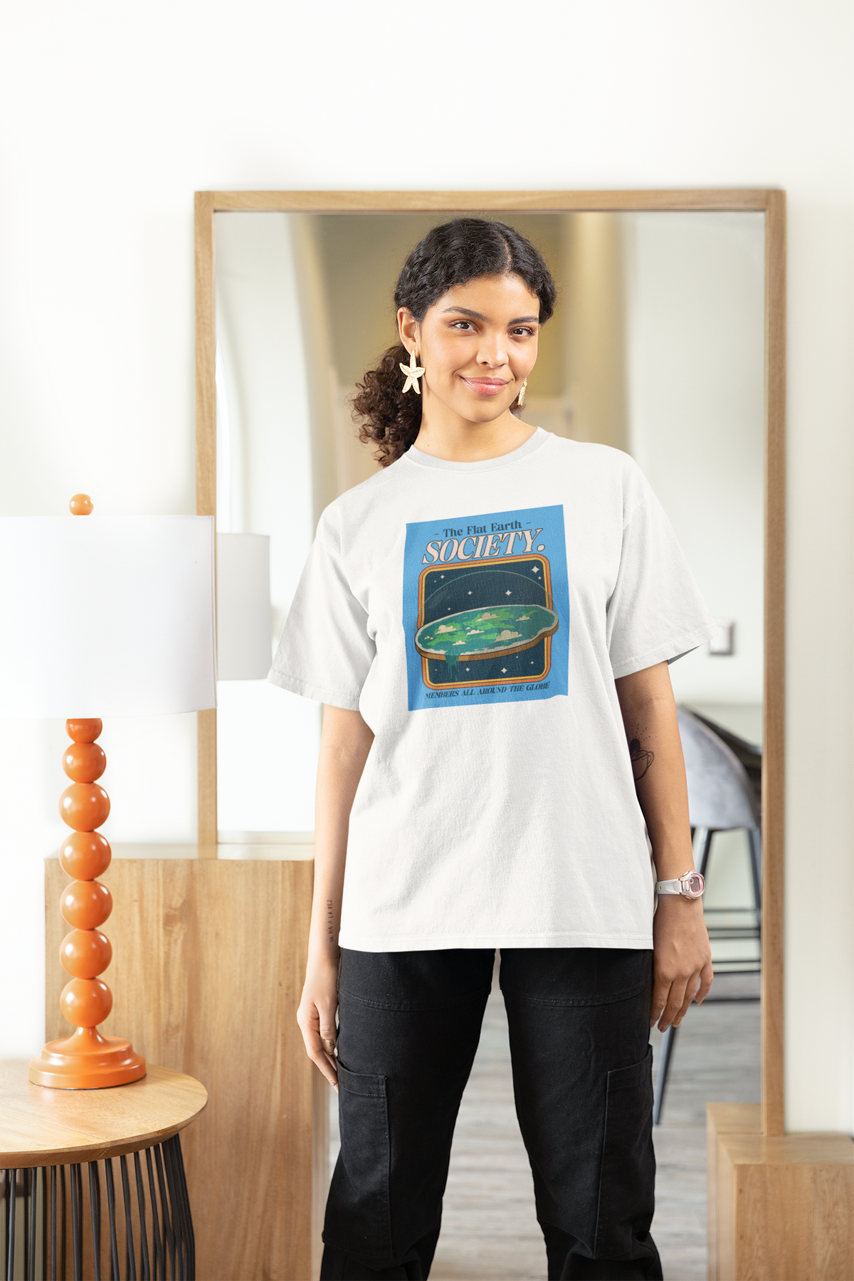 'The Flat Earth Society' women's tee in white, woman wearing it at home, funny satire gift idea
