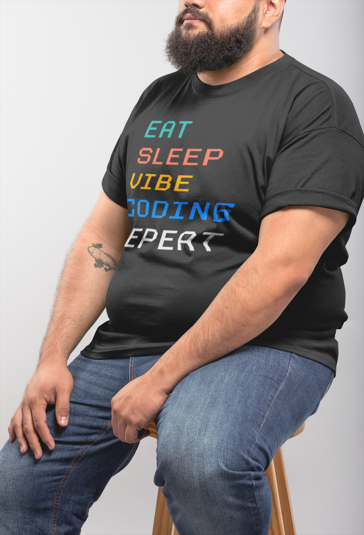 'Eat Sleep Vibe Coding Repeat' t-shirt in black, bearded man wearing it seated, funny gift for developers
