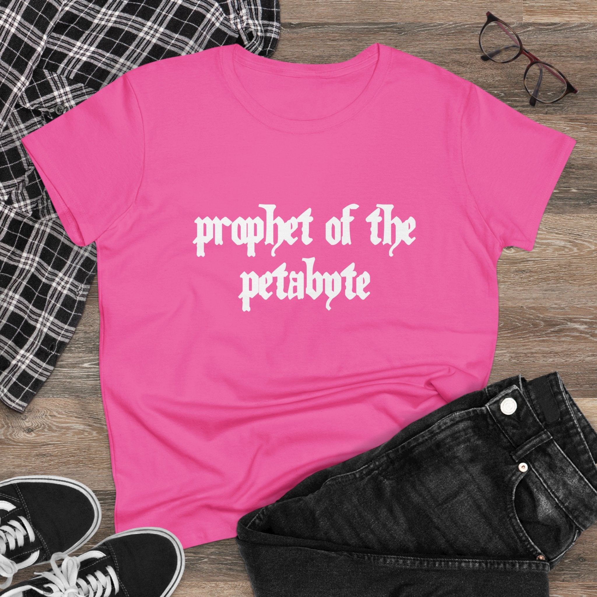 The "Prophet of the Petabyte" Women's Tee, crafted from soft cotton and featuring its slogan in white, pairs effortlessly with black jeans, a plaid shirt, black sneakers, and glasses laid out on a wooden floor.