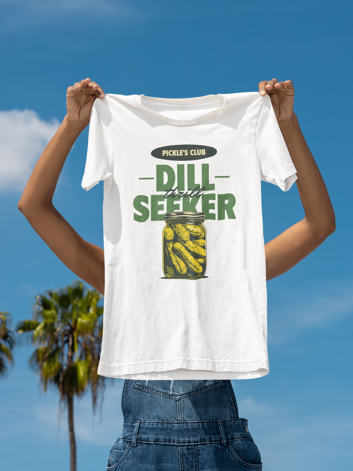 'Dill Seeker' pickle jar pun t-shirt in white, man holding it up outdoors under palm trees, funny gift