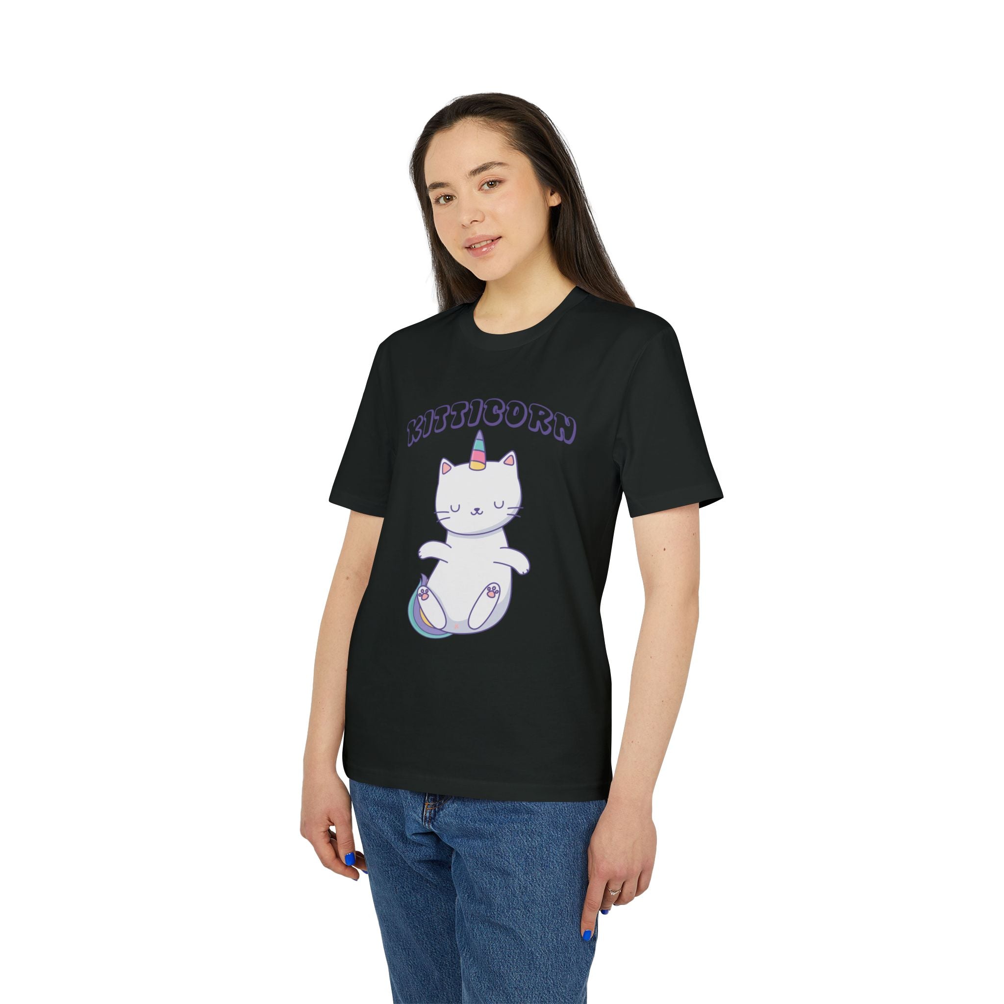 A woman wears the Organic T-Shirt - Kitticorn Design, which features a white cat with a unicorn horn and "Kitticorn" above it, paired with blue jeans—a whimsical gift for cat lovers and fans of playful style.