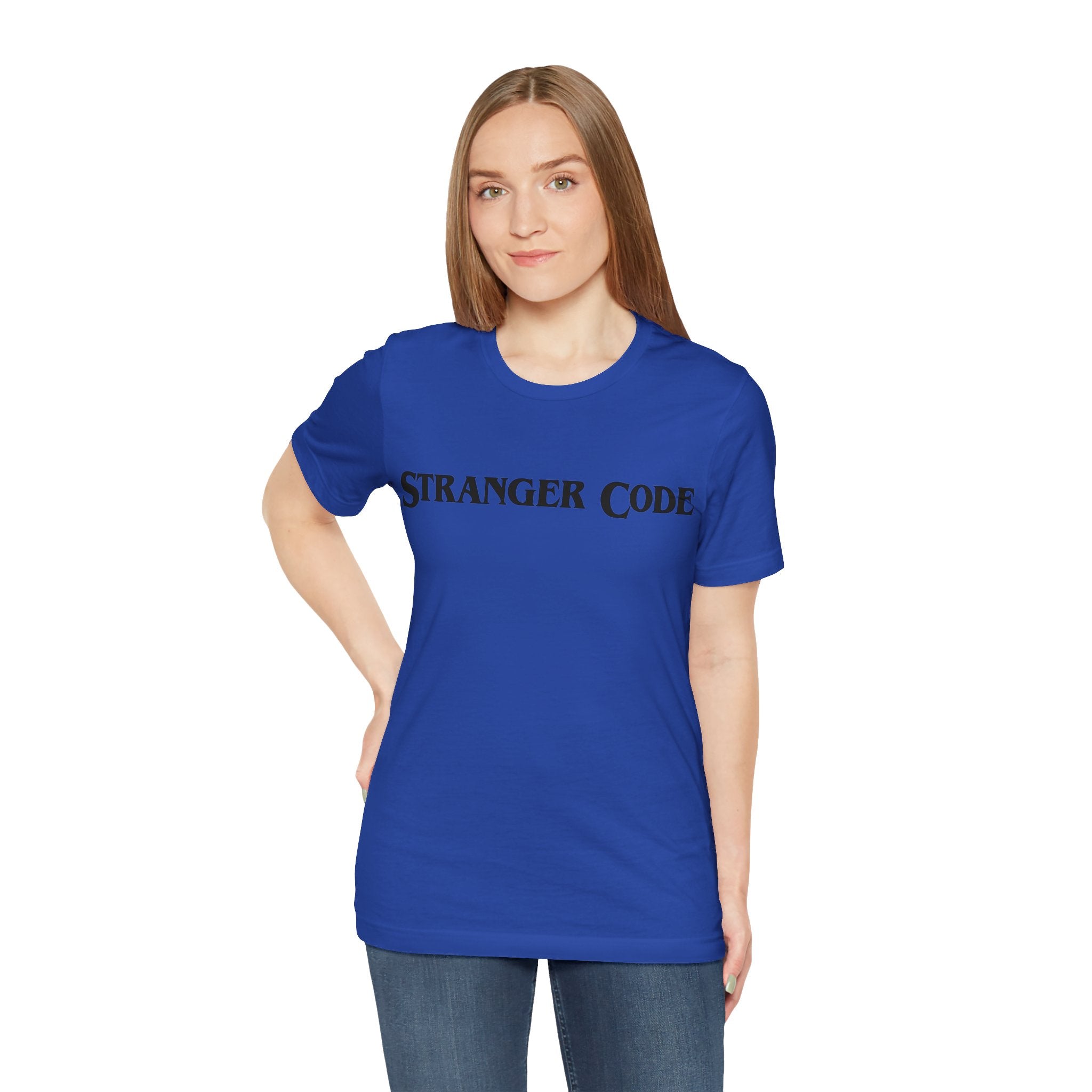 A person wearing the Stranger Code Tee Shirt, a classic unisex jersey crafted from soft cotton and adorned with the quality "STRANGER CODE" print, stands against a plain background, looking toward the camera with one hand on their hip.