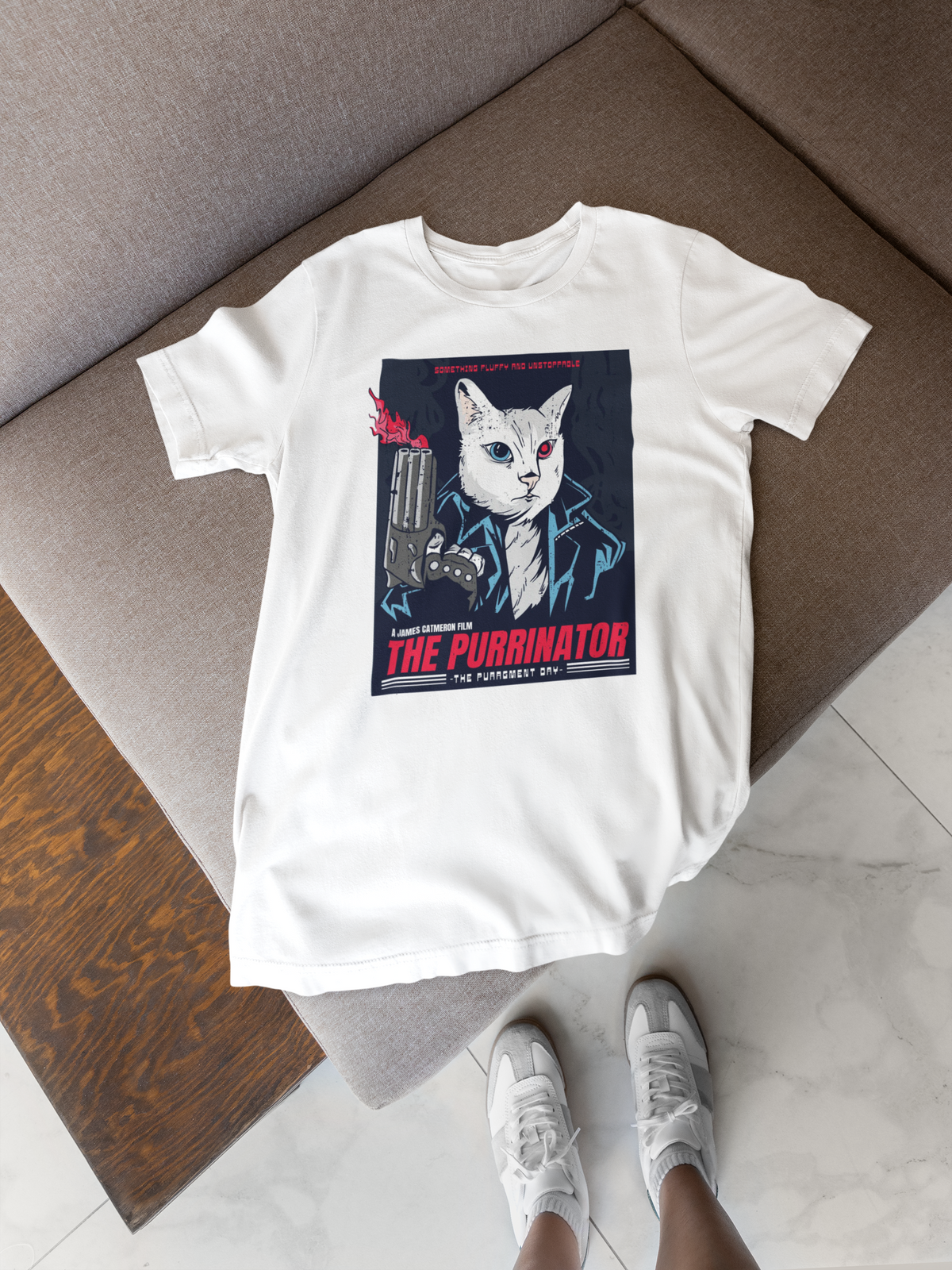 'The Purrinator' t-shirt in white, flat lay on a wooden floor with sneakers, funny movie parody cat gift