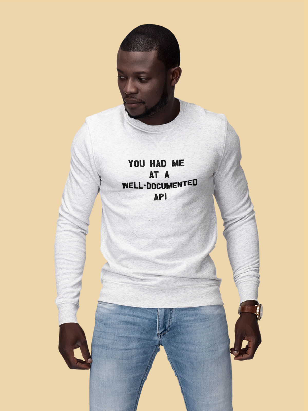"You Had Me At A Well-Documented API" sweatshirt in white, man wearing it on tan backdrop, funny coder gift