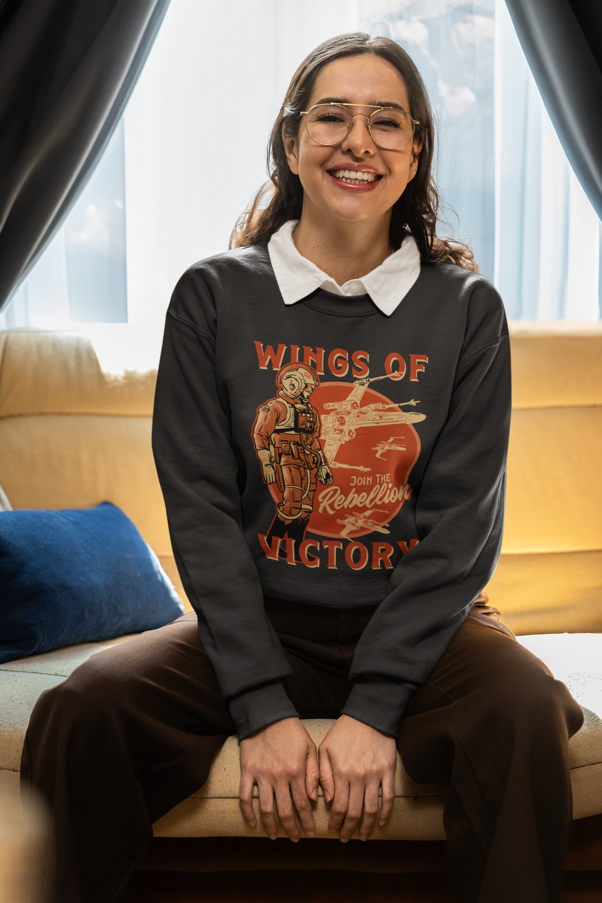 'Wings of Victory' sweatshirt in black, woman sitting wearing it indoors, warrior graphic sweatshirt