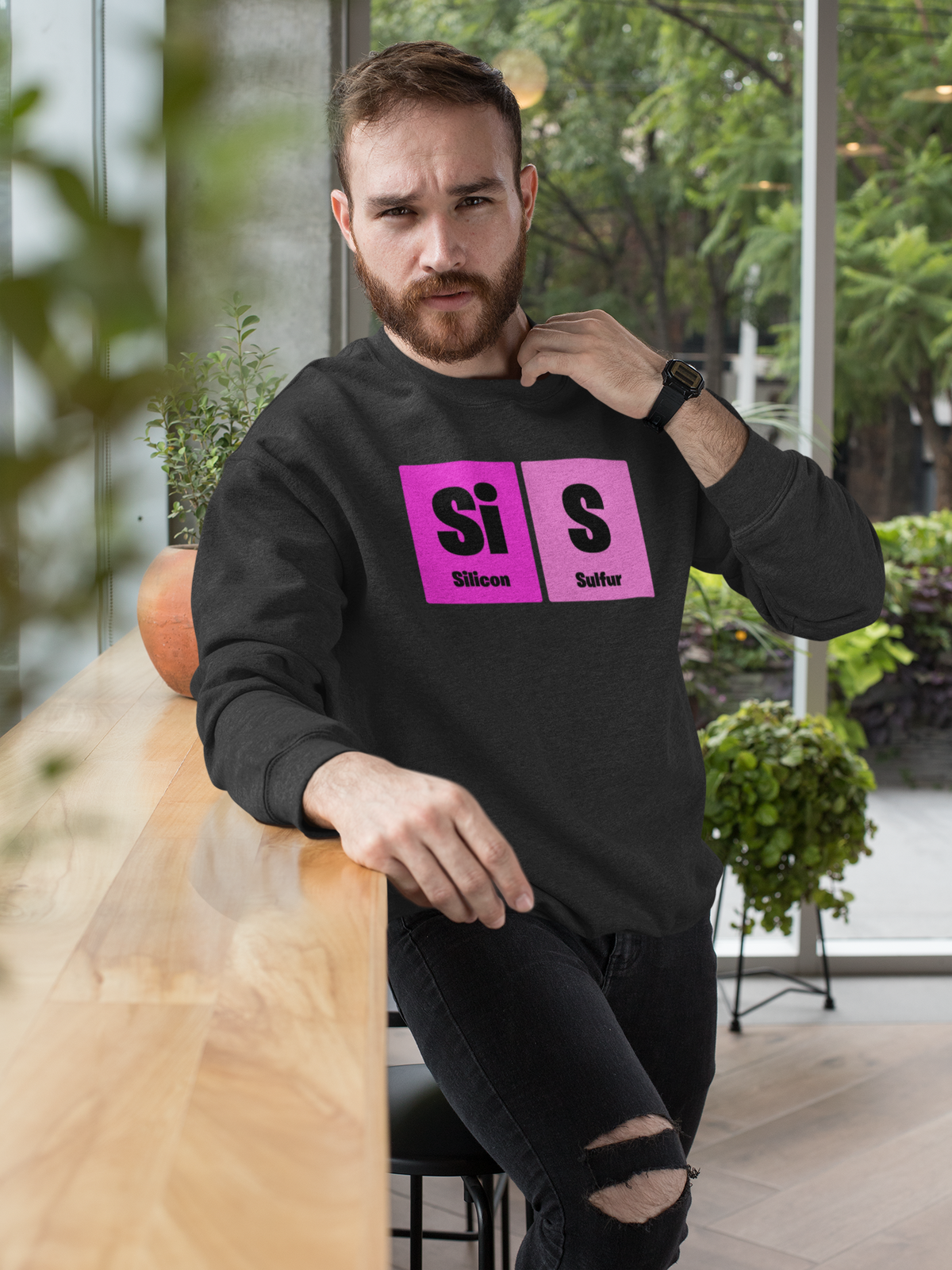 'Sis' periodic table sweatshirt in black, man sitting outdoors wearing it, casual lifestyle photo