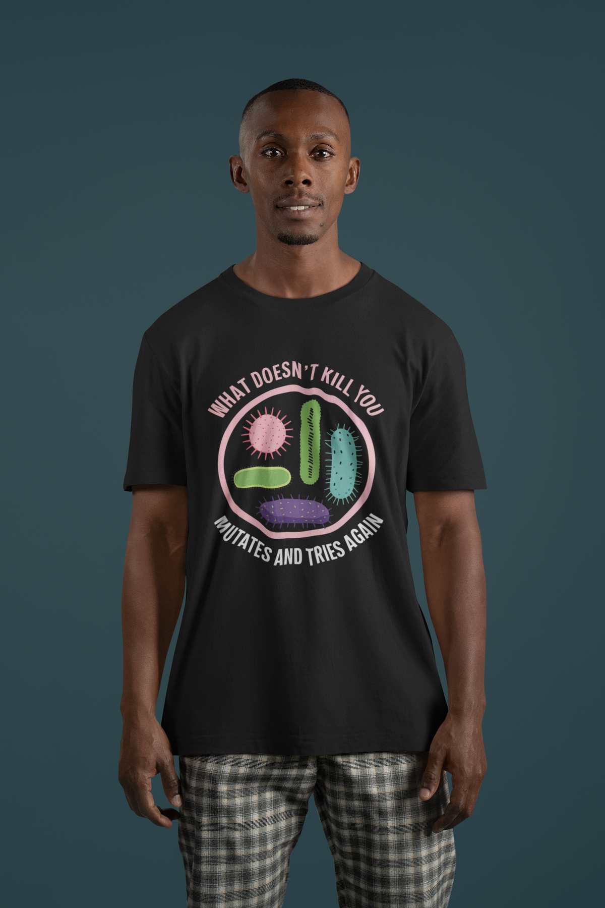'What Doesn't Kill You' virus graphic t-shirt in black, man wearing it, teal backdrop, biology gift