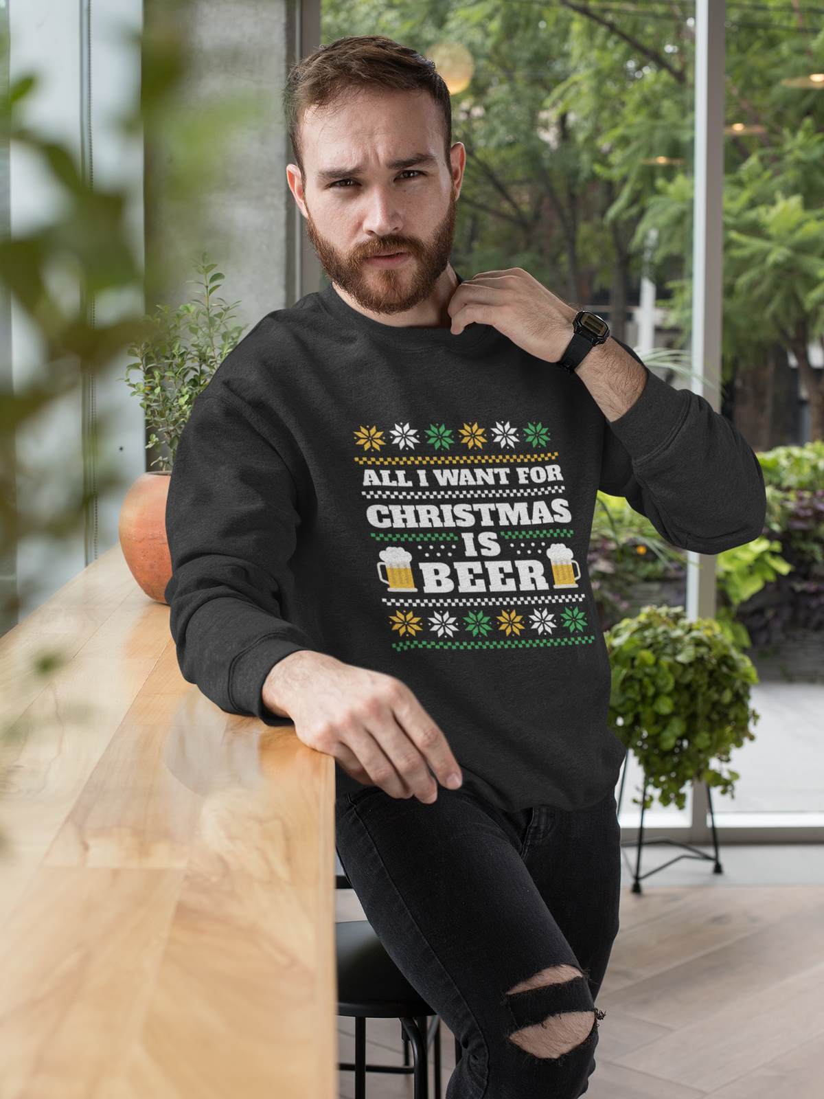 'All I Want For Christmas Is Beer' crewneck in black, bearded man wearing it by plants, funny holiday gift