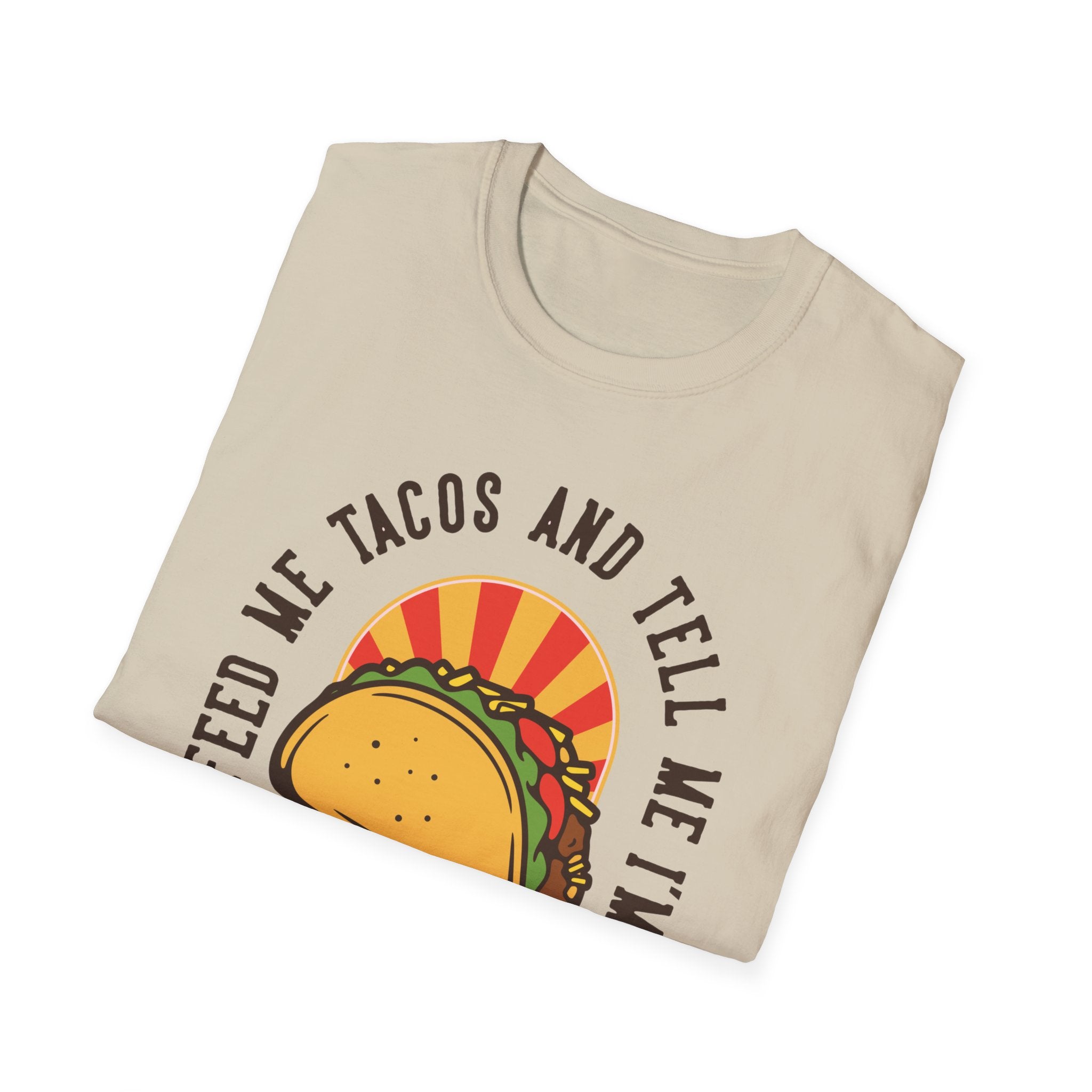 A folded beige T-shirt titled "Feed Me Tacos and Tell Me I'm Pretty" showcases a taco illustration, making it an ideal choice for Taco Tuesday enthusiasts who want to express their love for tacos with style.