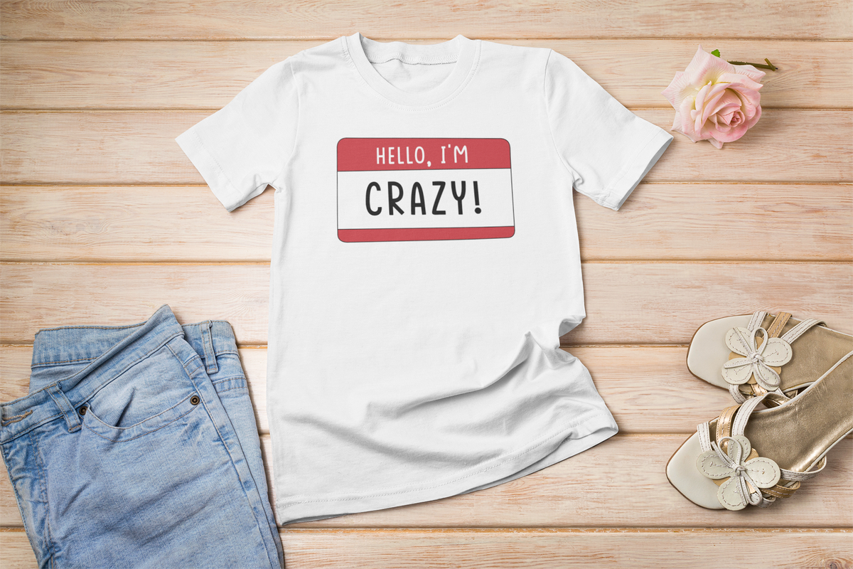 Hello I'm Crazy name tag T-shirt in white, flat lay styled with roses and sandals, funny sarcastic tee