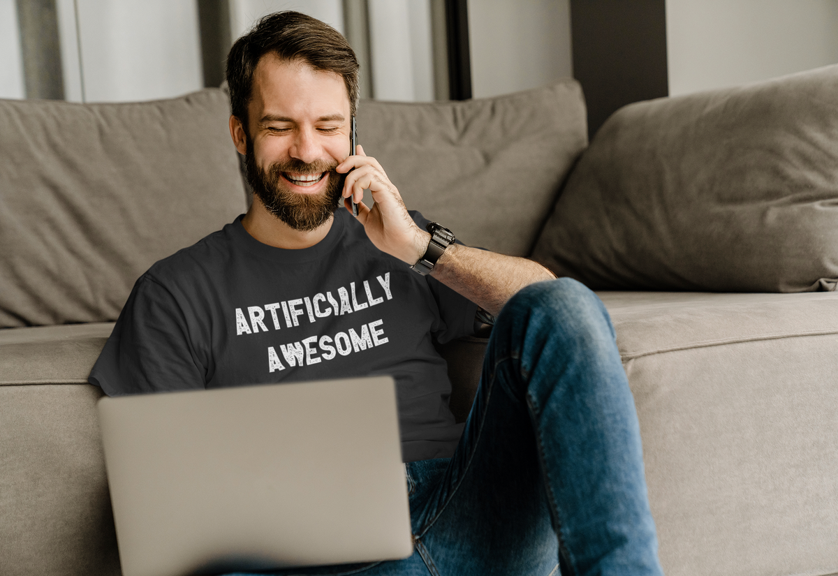 'Artificially Awesome' t-shirt in black, man wearing it on couch on phone, cozy funny AI lover gift