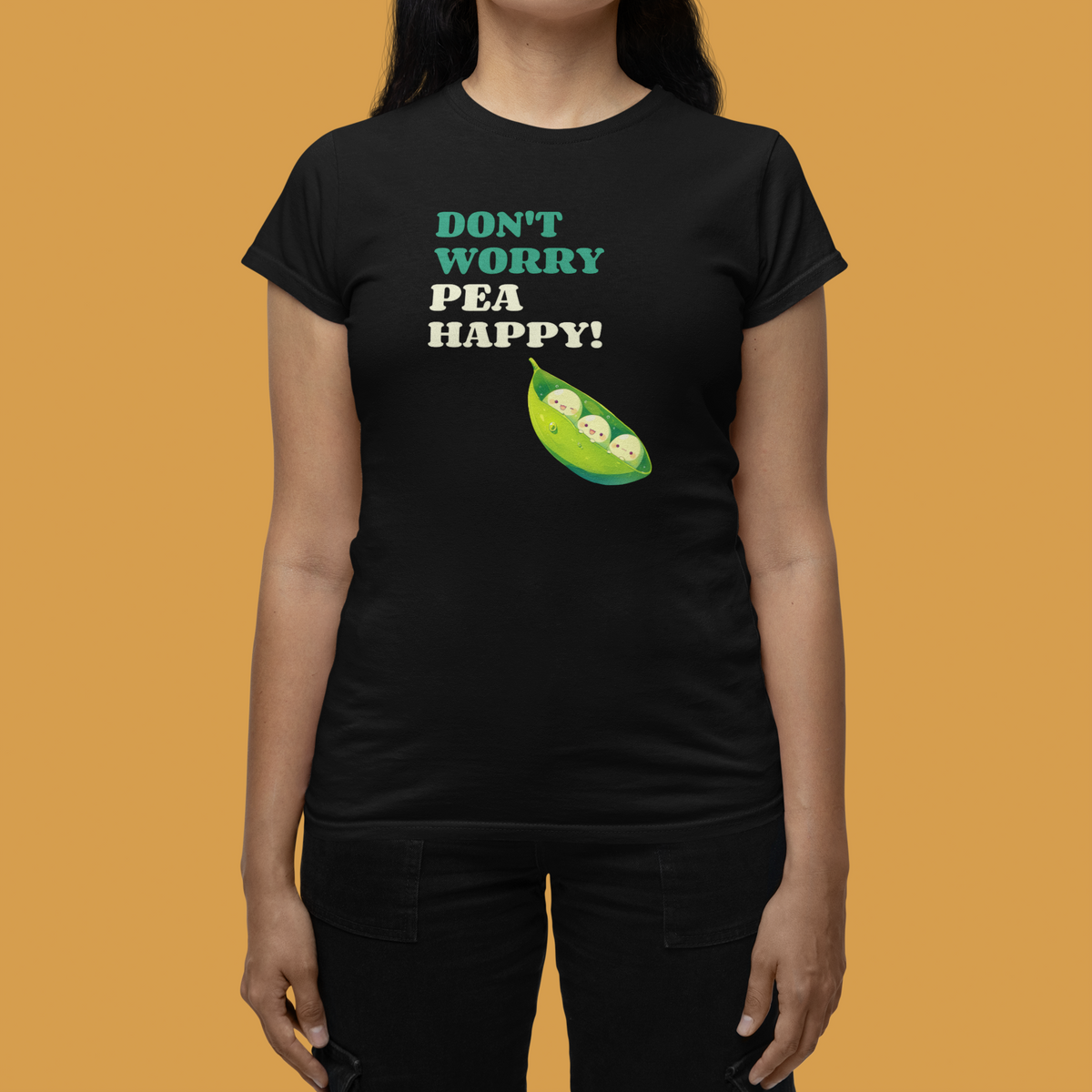 'Don't Worry Pea Happy' pea pun women's tee in black, close-up on woman, mustard backdrop, veggie gift