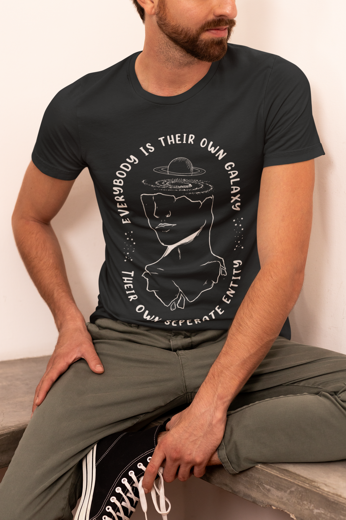 "Everybody Is Their Own Galaxy" graphic t-shirt in black, bearded man wearing it side view, unique science pun gift