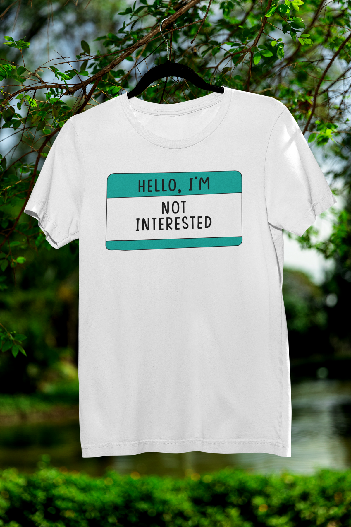 Hello I'm Not Interested name tag T-shirt in white, hanging outdoors among trees, funny sarcastic tee