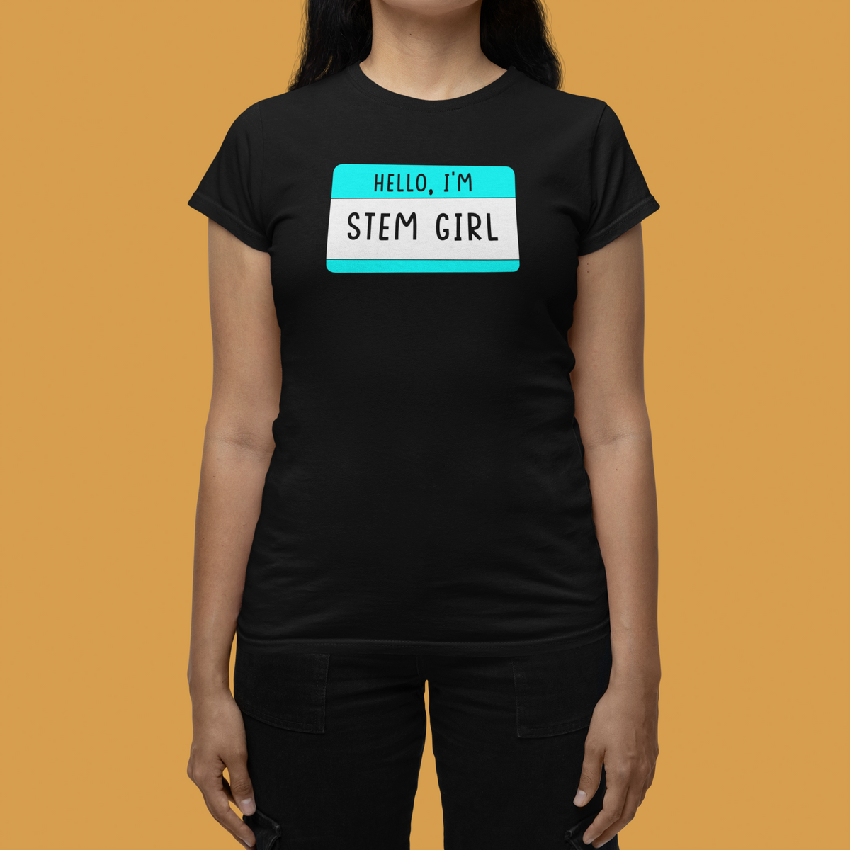Hello I'm Stem Girl name tag T-shirt in black, woman wearing it against an orange backdrop, science gift tee