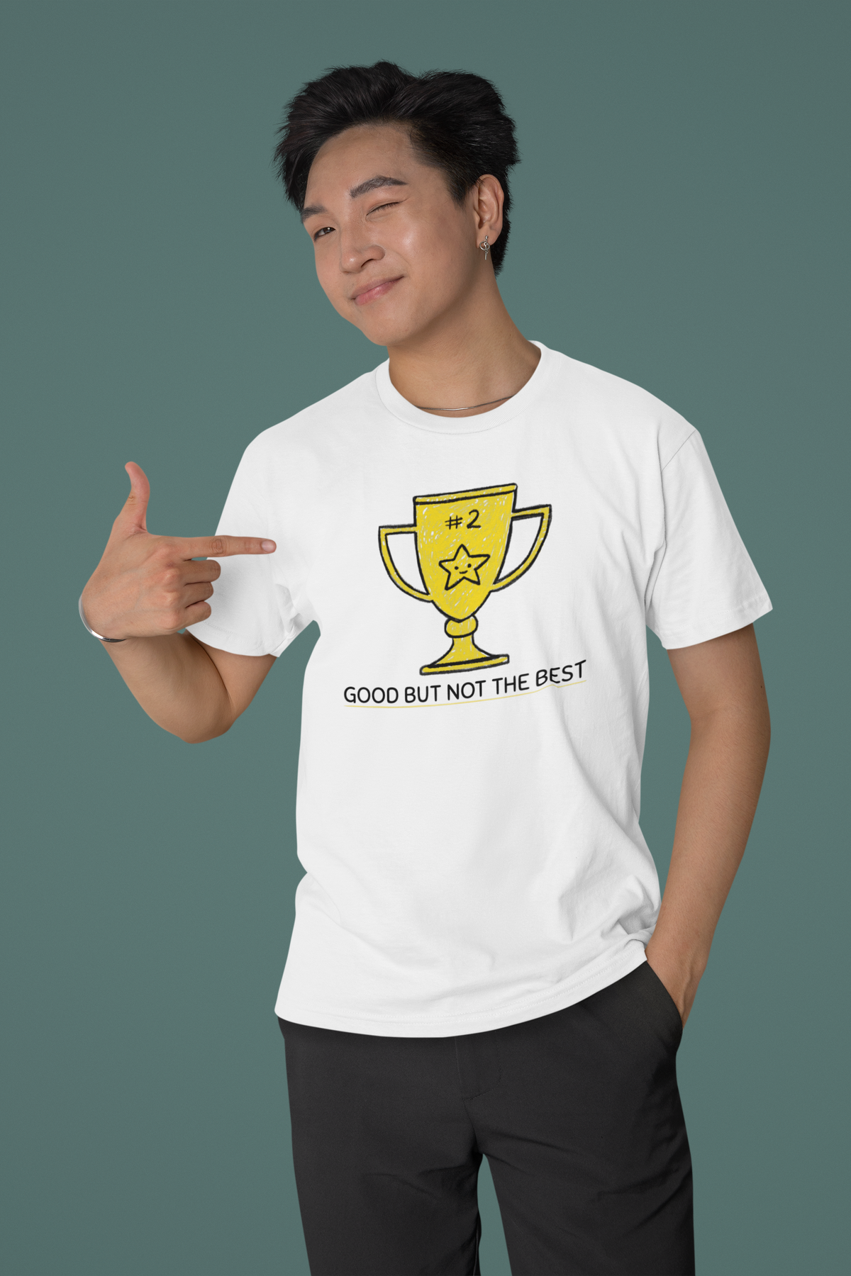 'Good But Not the Best' trophy tee in white, man pointing at print, studio backdrop, funny sarcastic t-shirt gift