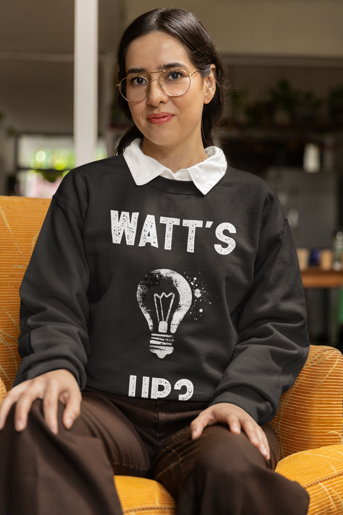 'Watt's Up?' sweatshirt in black, woman sitting indoors, funny electrician pun sweatshirt gift