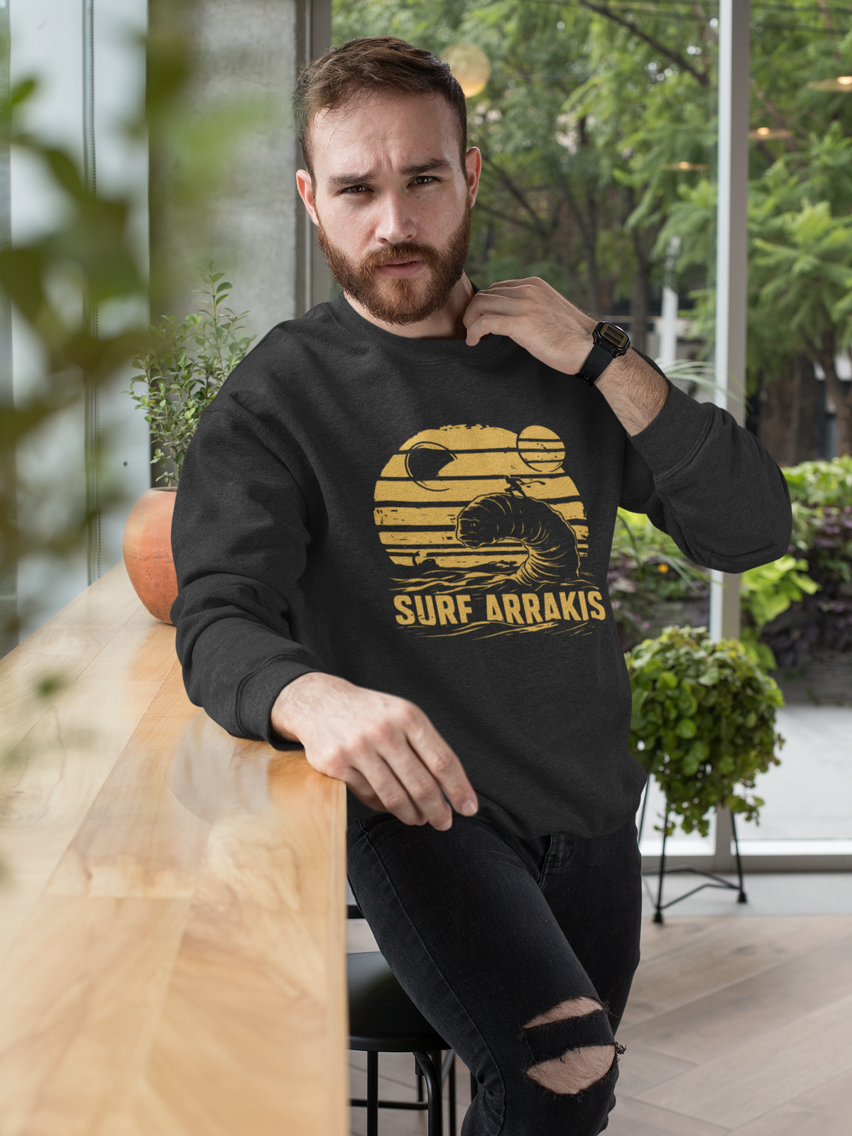 Surf Arrakis sandworm sweatshirt in black, bearded man wearing it outdoors by plants, funny sci-fi gift