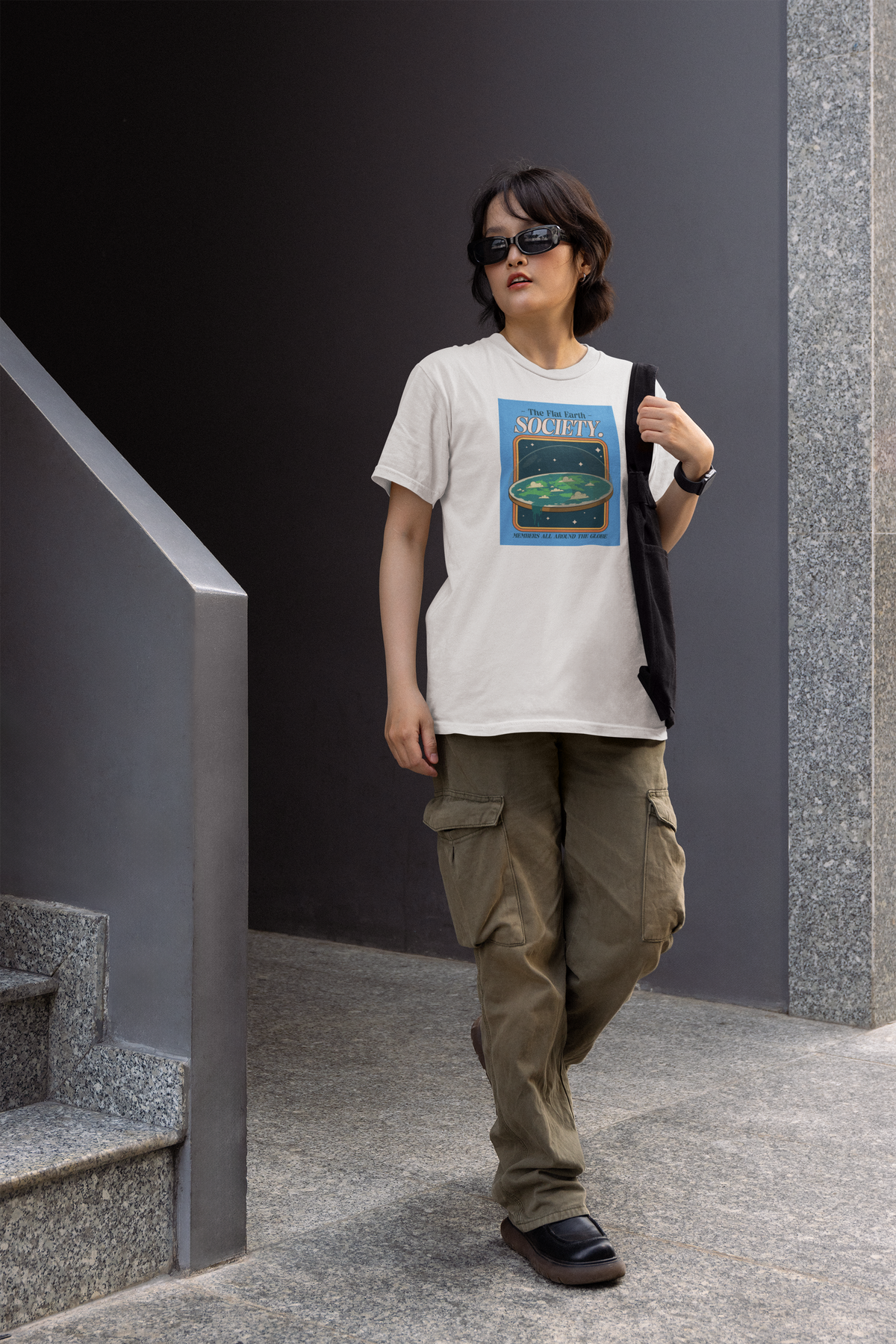 'The Flat Earth Society' women's tee in white, man wearing it outdoors, funny science satire gift