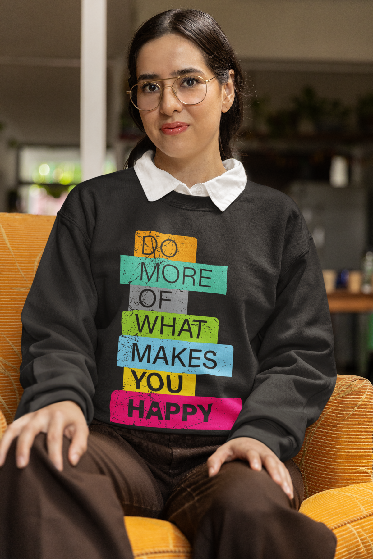 'Do More of What Makes You Happy' sweatshirt in black, woman sitting indoors wearing it, uplifting gift
