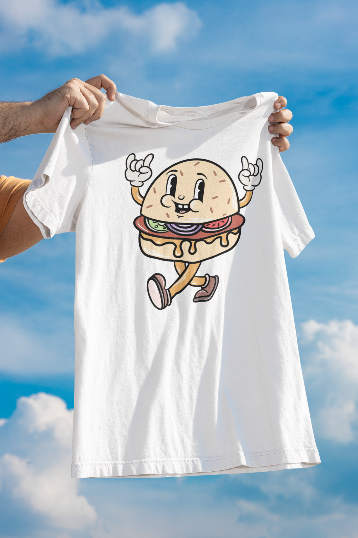 Cartoon burger t-shirt in white, held up outdoors against a cloudy sky, funny foodie gift