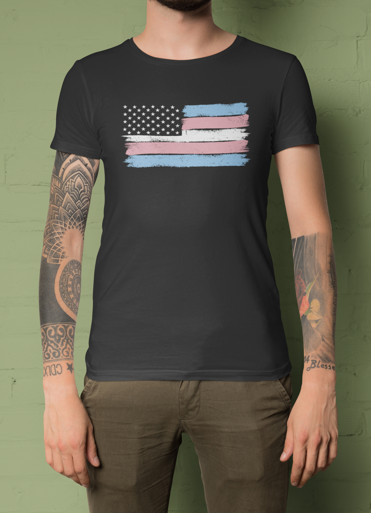 Trans pride flag t-shirt in black, tattooed man model wearing it against a green background