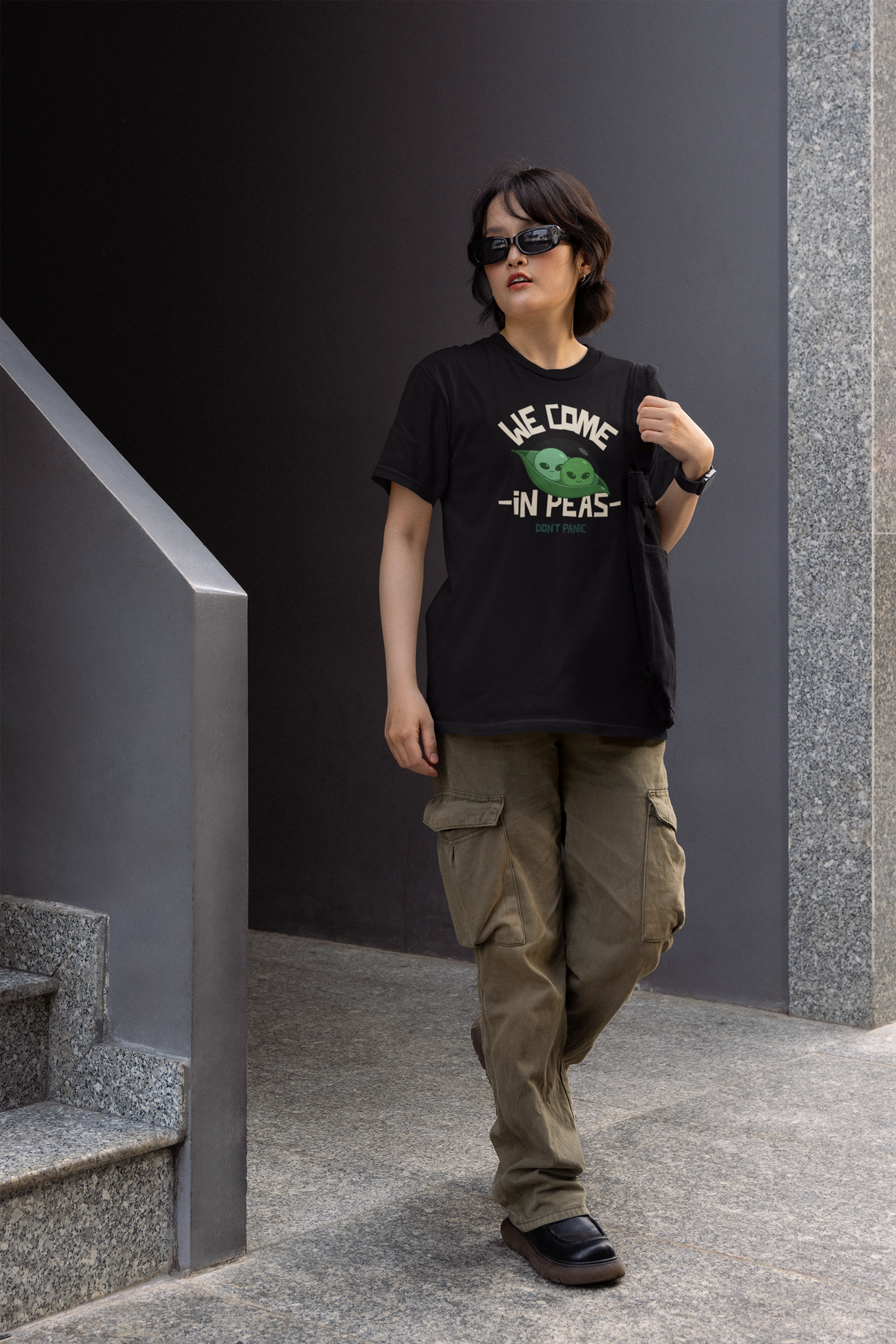 'We Come in Peas' t-shirt in black, person wearing it outdoors on stairs, funny sci-fi pea pun gift