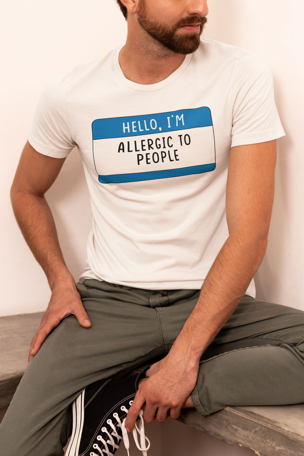 Hello I'm Allergic to People T-shirt in cream, man sitting cross-legged wearing it, sarcastic gift tee