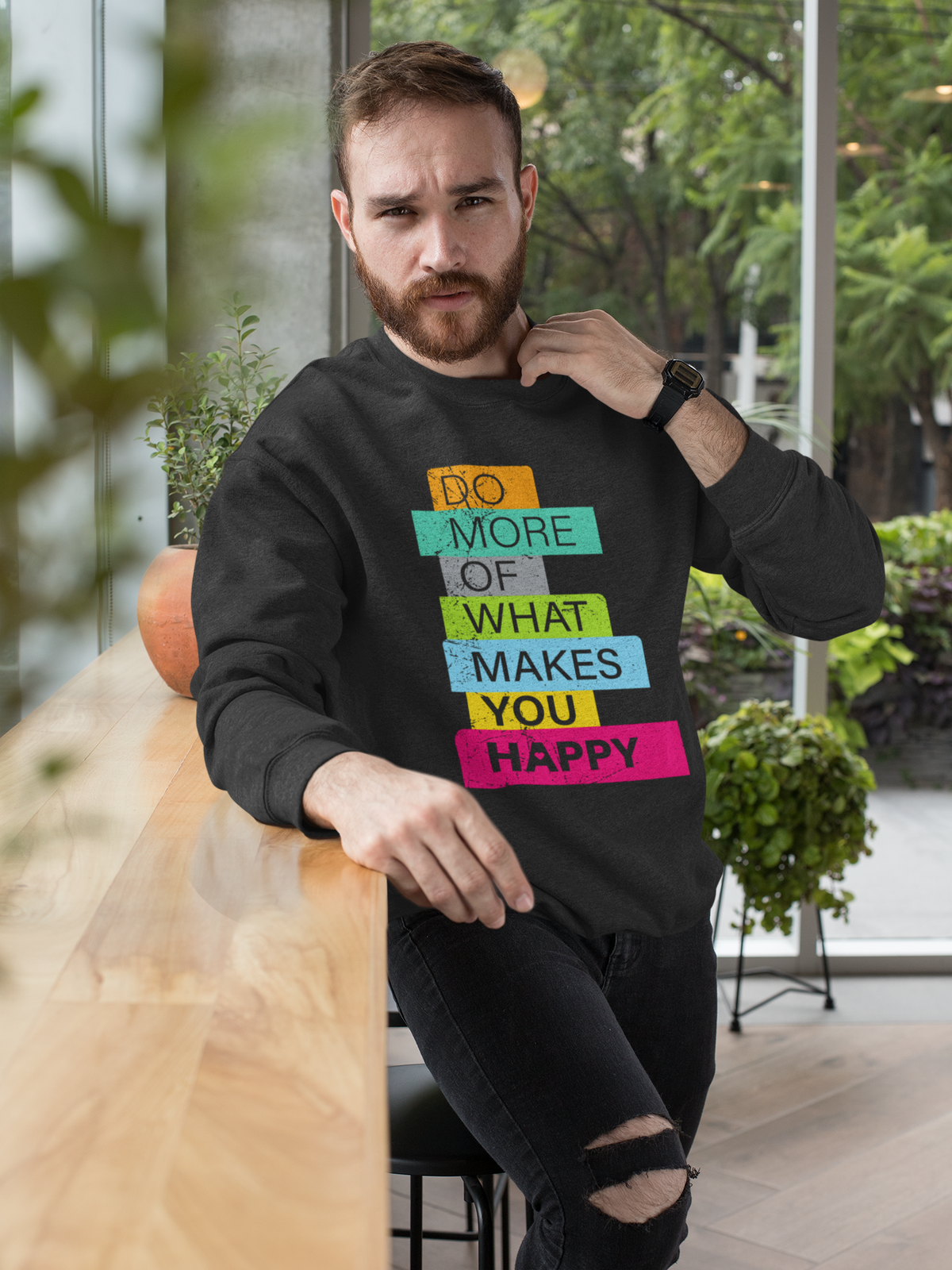 'Do More of What Makes You Happy' sweatshirt in black, bearded man wearing it at a cafe table, gift