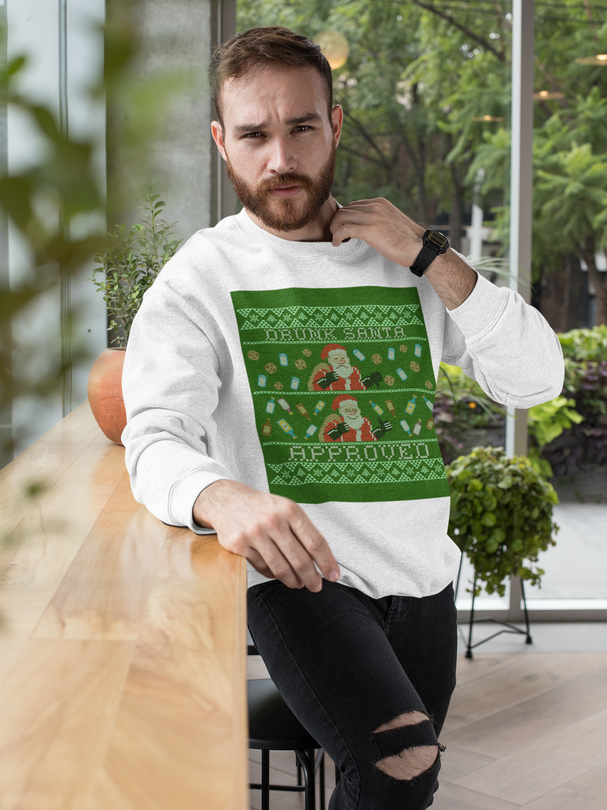'Drunk Santa Approved' ugly christmas sweatshirt in white, man sitting wearing it outdoors, funny gift