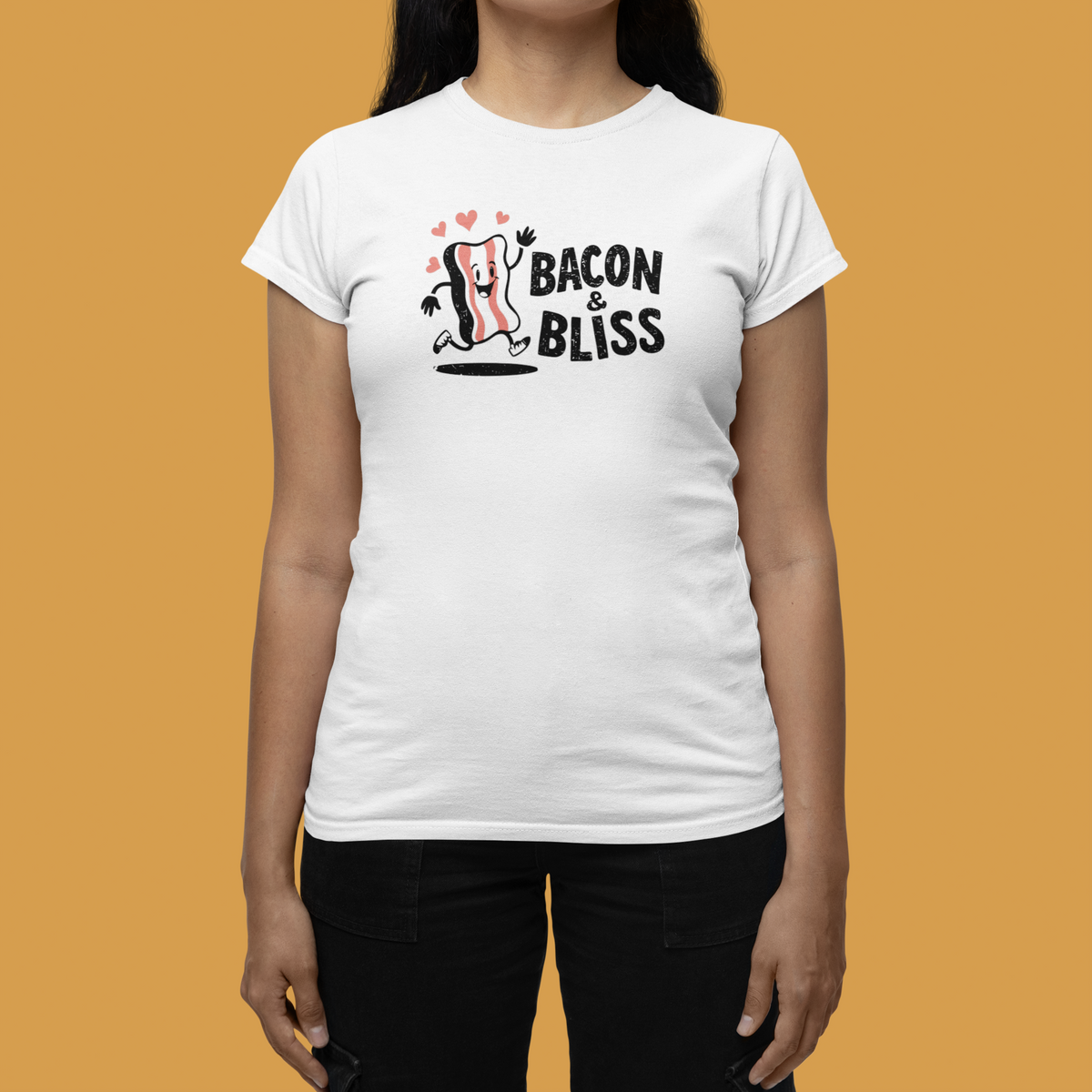 'Bacon & Bliss' womens tee in white with bacon character print, woman wearing it on mustard background, foodie gift