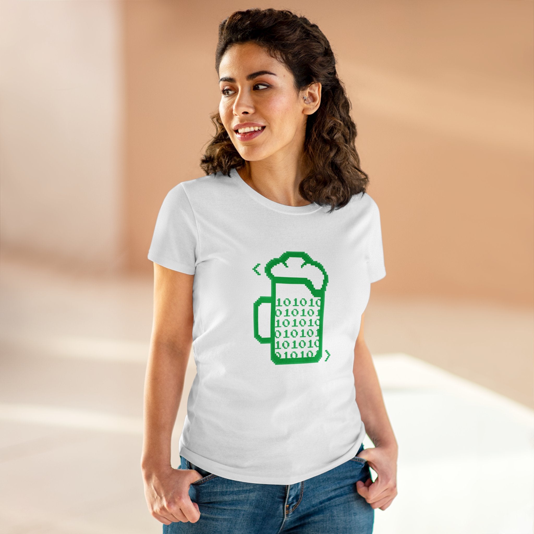 A woman wearing the Beer Code - Women's Tee, a geeky shirt with a green beer mug filled with binary code, stands indoors with one hand in her pocket.