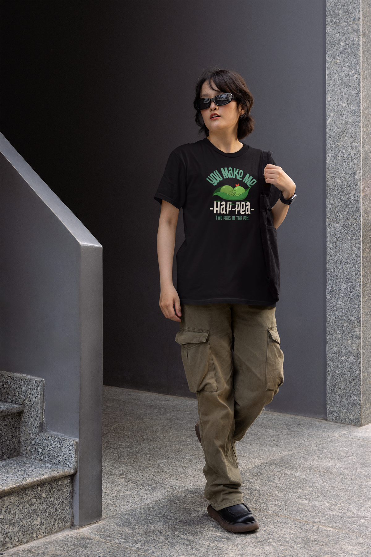 'You Make Me Hap-Pea' women's t-shirt in black, woman wearing it walking in an urban setting, funny pea pun tee