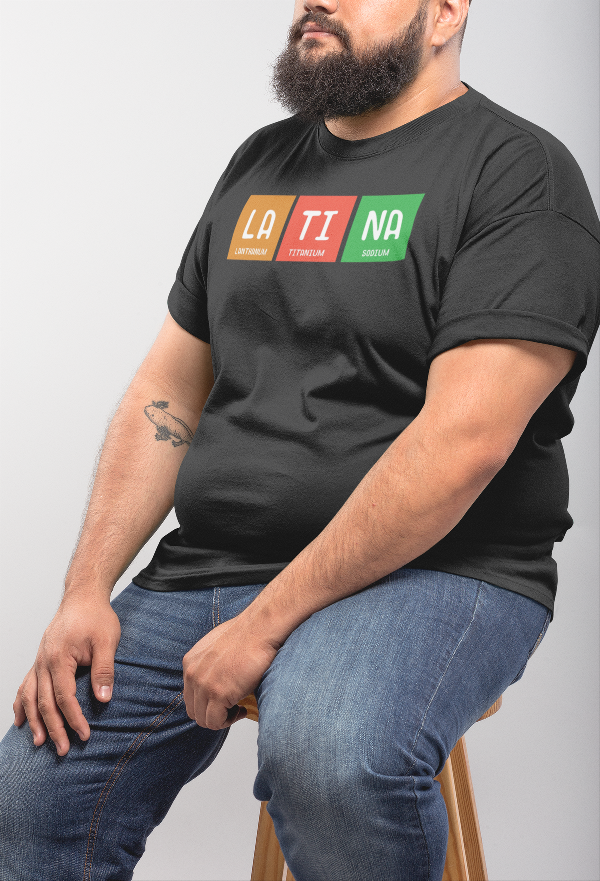 LA-TI-NA periodic table t-shirt in black, heavyset bearded man wearing it seated, funny gift