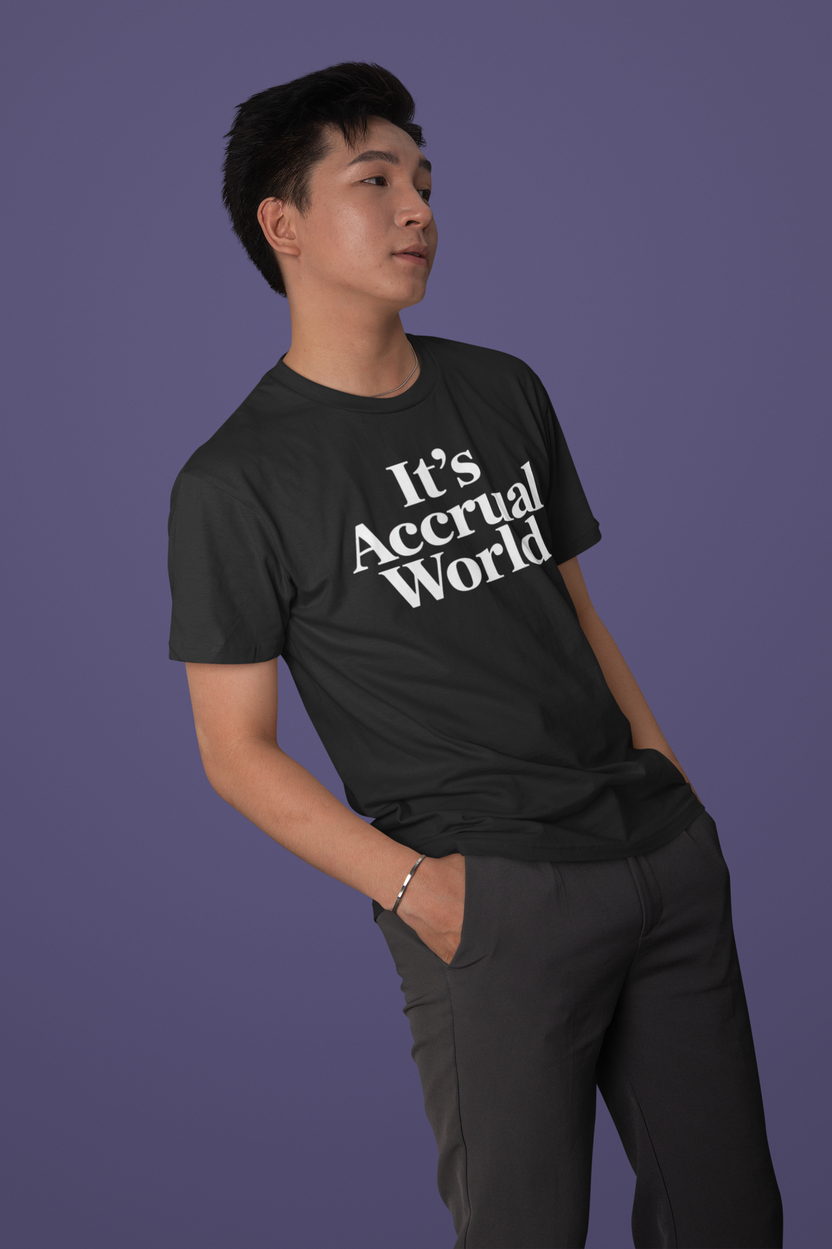 'It's Accrual World' t-shirt in black, man leaning against wall on purple background, accountant gift