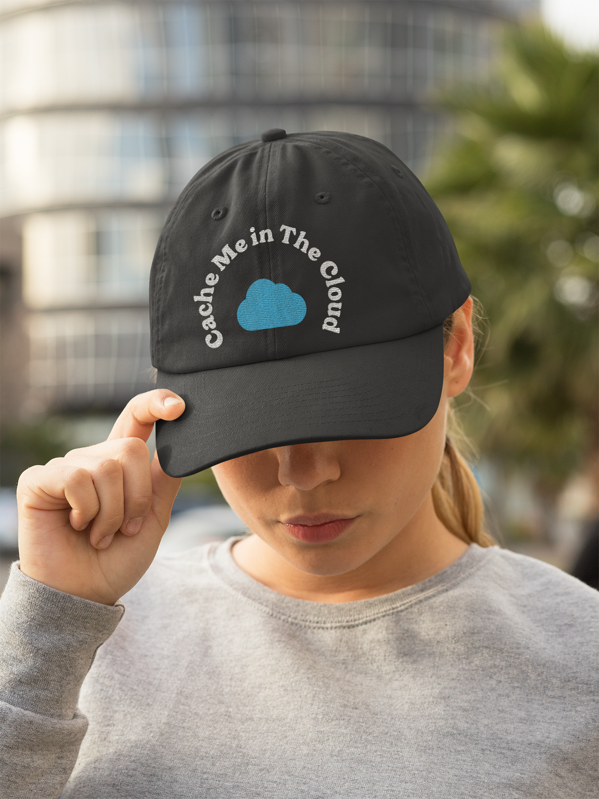 'Cache Me in The Cloud' dad hat in black, woman wearing it outdoors in the city, funny gift for programmers